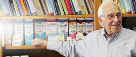 Lactaid founder, Alan Kilgerman, standing in an office pointing to Lactaid product packaging