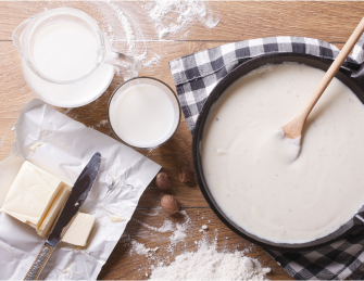 White sauce recipe in a pan with flour, milk and butter on the side
