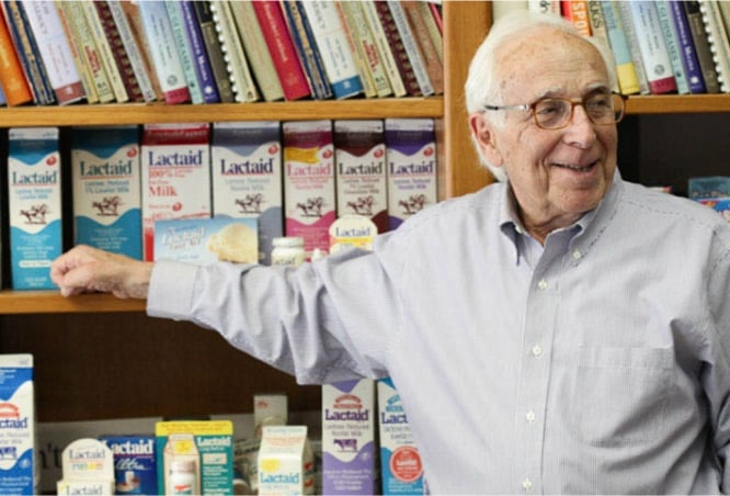 El fundador de la marca LACTAID, Alan Kilgerman, parado en una oficina apuntando al envoltorio del producto LACTAID 
