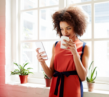 A black young woman drinking in a cup and holding a cellphone in her hand