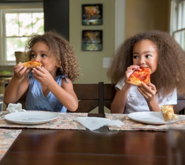 Two little girls eating pizza.