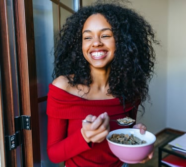 Woman smiling as she eats a bowl of cereal.