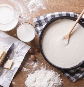 White sauce recipe in a pan with flour, milk and butter on the side.