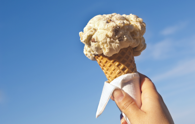 A hand holding and ice cream cone with the sky as background