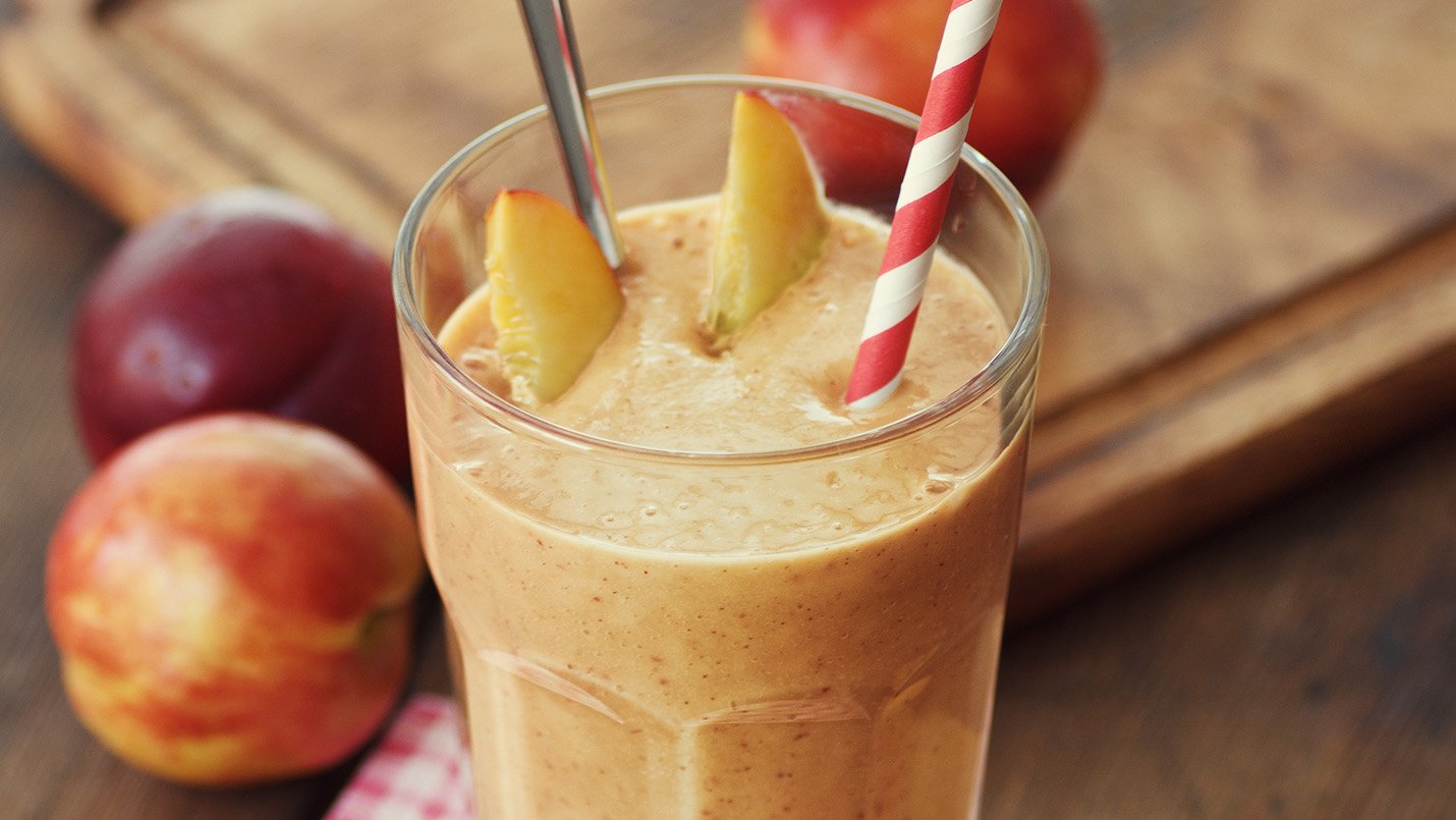 Healthy peach smoothie with spoon and red straw