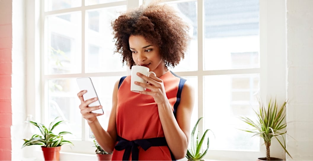 woman drinking out of cup while checking phone