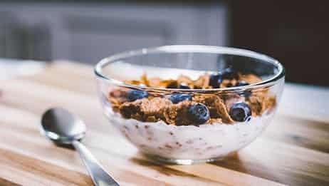 Cereal and blueberries with milk in a bowl with a metal spoon on a wooden table