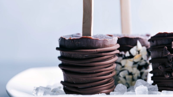 Frozen dark chocolate pudding popsicles with different garnishes like extra chocolate and nuts